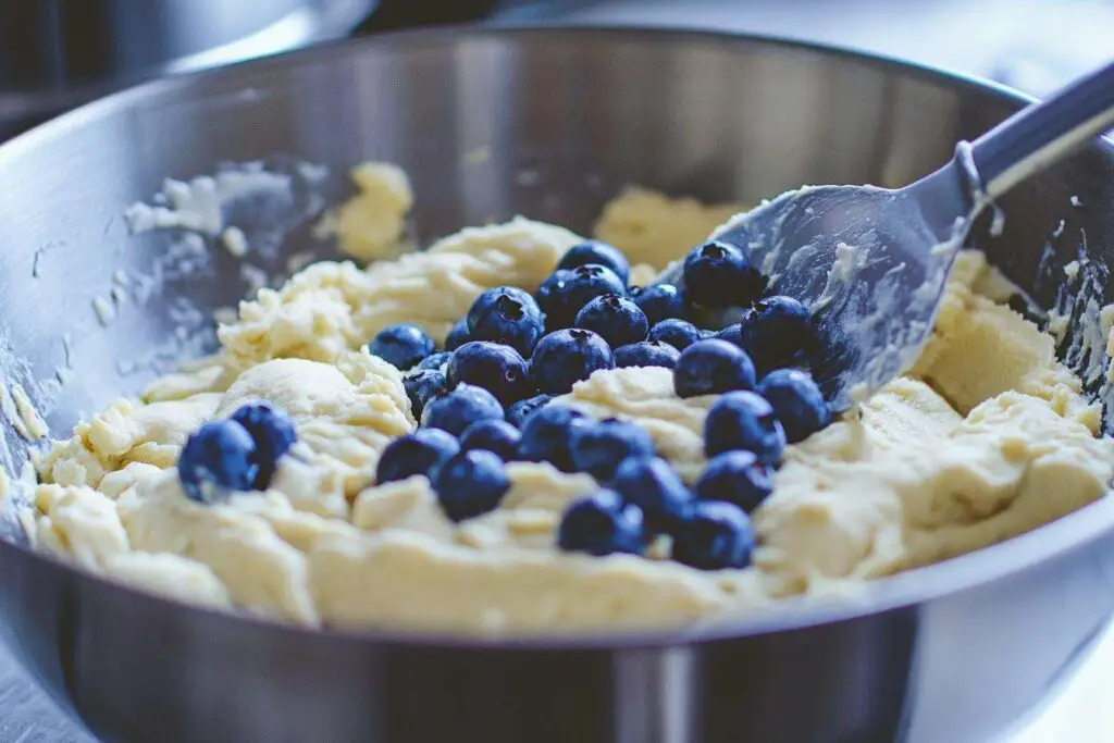 Cookie Dough With Blueberries Being Folded In By A Spatula In A Mixing Bowl